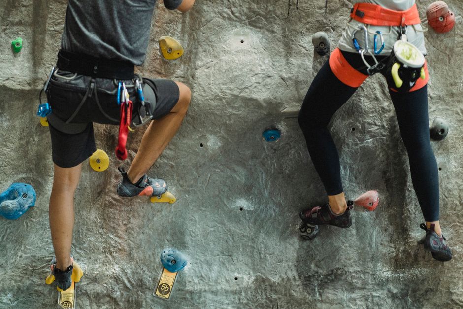 Back view of crop anonymous couple in activewear climbing on gray rocky wall