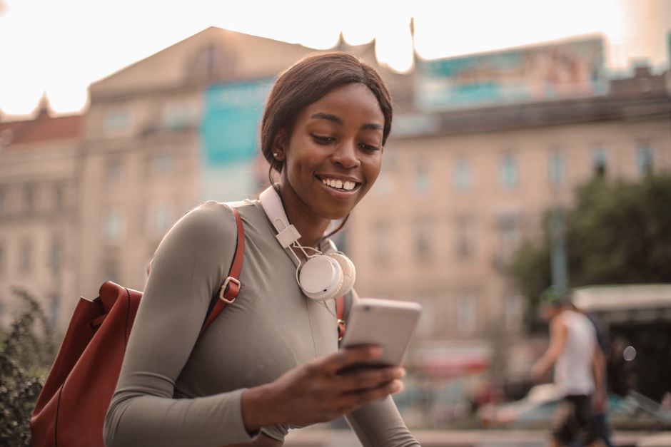 Smiling woman with smartphone and headphones enjoying leisure outdoors.