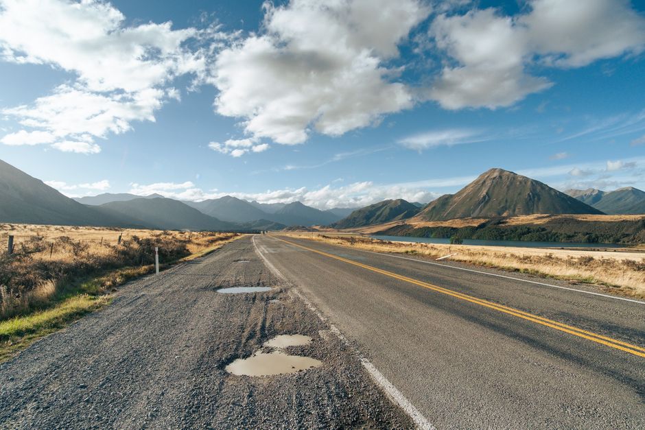 Idyllic mountain road near Lake Pearson, Canterbury, showcasing clear skies and rugged landscape.