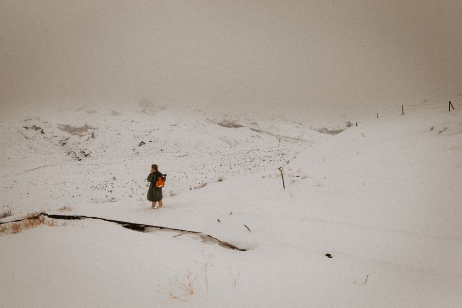 A lone hiker treks through a vast, snowy mountain under a cloudy sky.