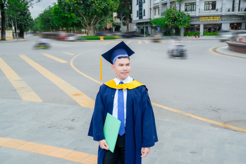 A young graduate stands proudly in cap and gown outdoors, celebrating academic achievement.