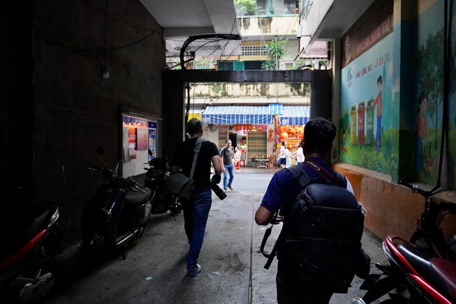 Two photographers walk down a lively city alley capturing street life.