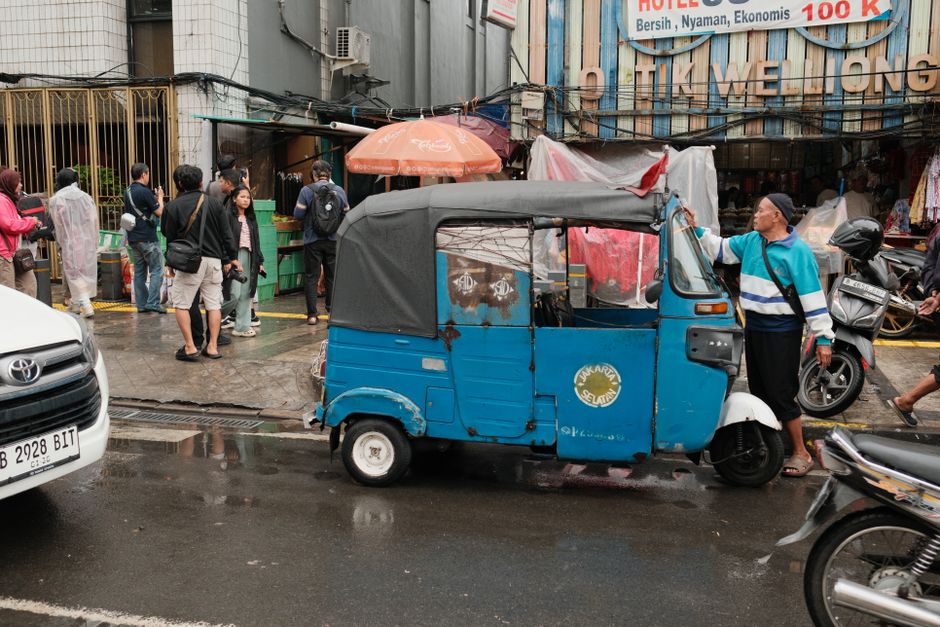 An outdoor market scene in Jakarta featuring a traditional bajaj and local people.