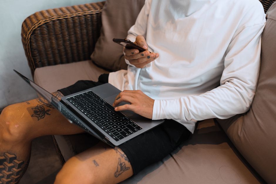 Young man uses laptop and smartphone while sitting on a couch indoors.