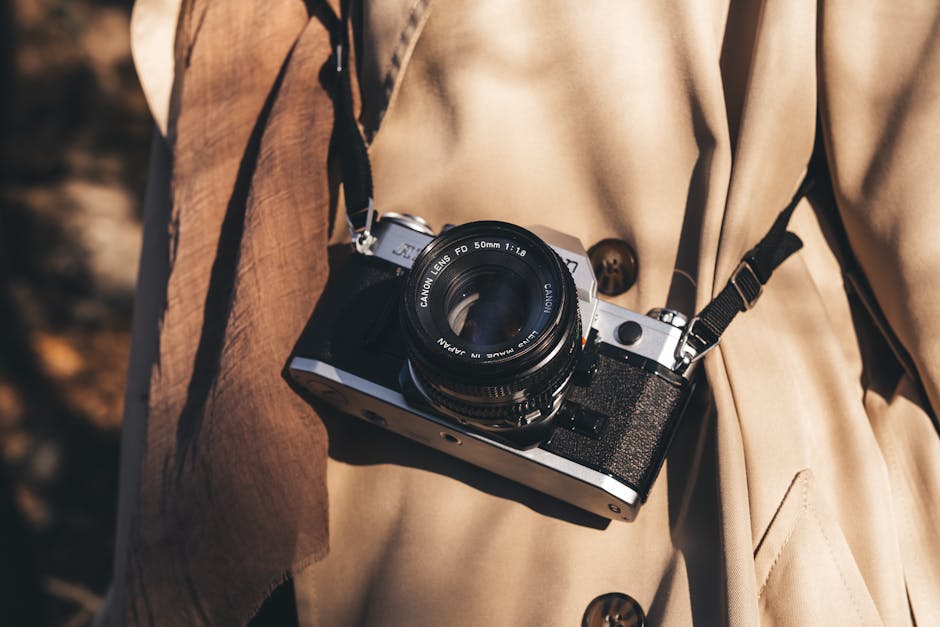 Close-up of a vintage camera hanging on a beige coat outdoors in autumn sunlight.