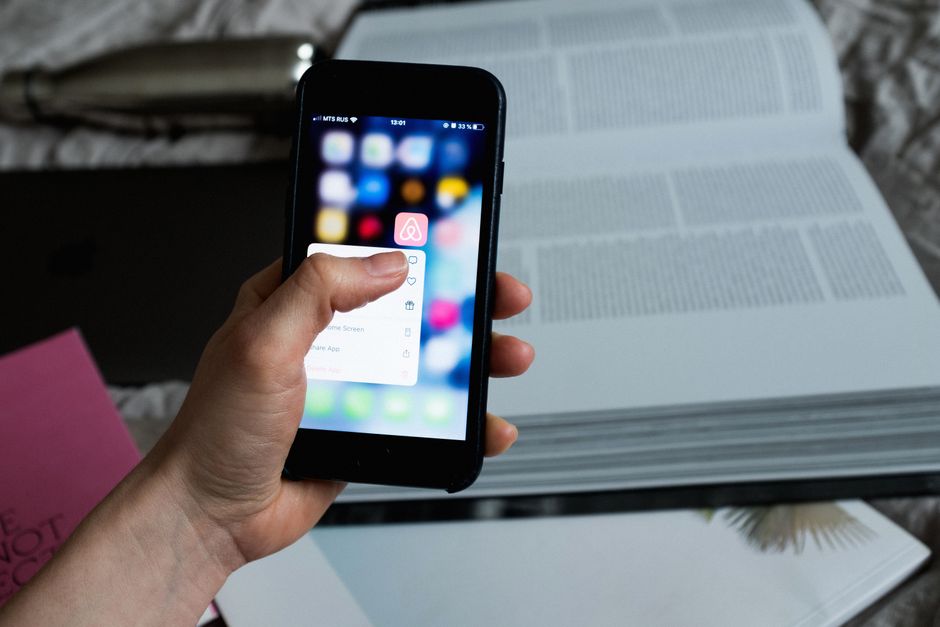 Crop faceless person choosing option from pop up window app while using cellphone and having open book located on bed sheet