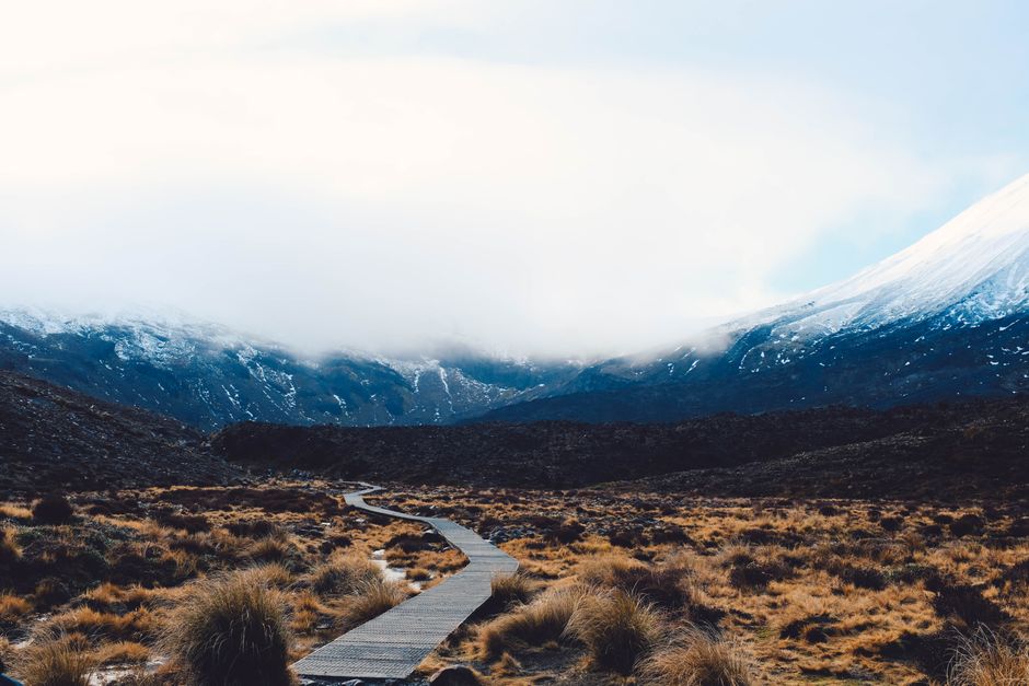 Explore a tranquil wooden pathway leading through a snow-capped mountain landscape under a cloudy sky.