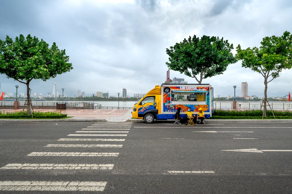 Colorful food truck parked along a scenic riverside street on a cloudy day.