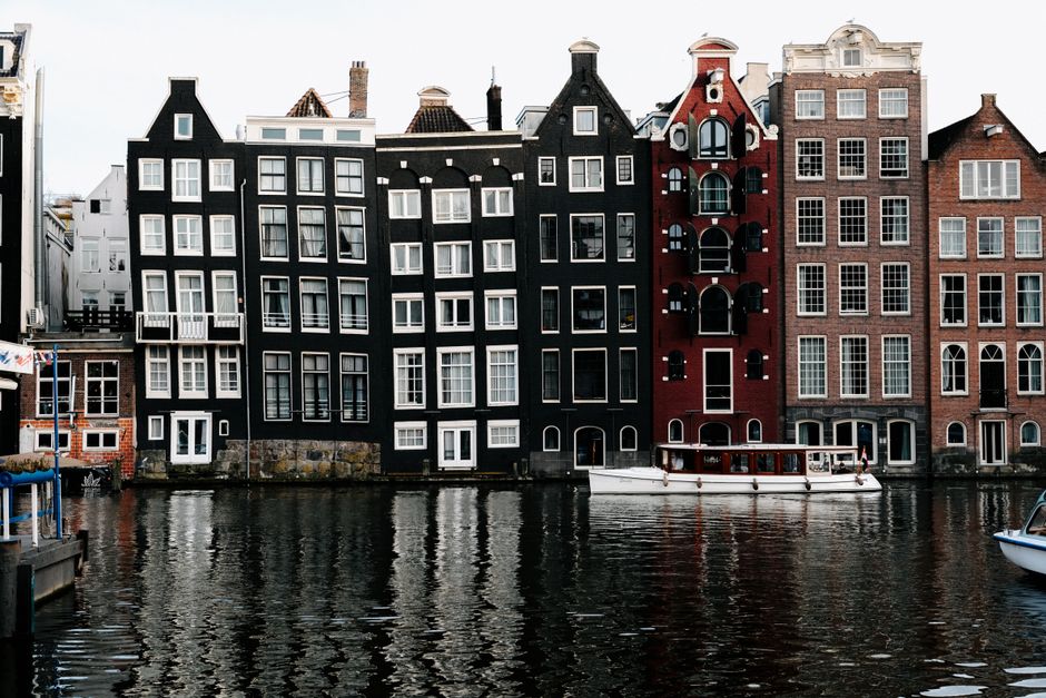 Stunning view of Amsterdam's iconic canal houses reflecting on water, showcasing unique architecture.