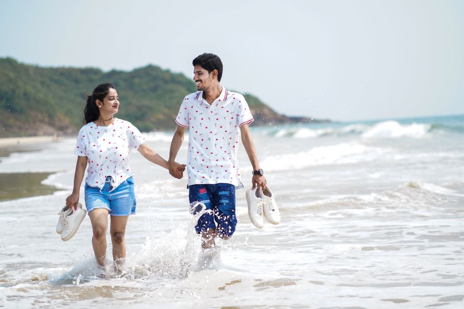 A cheerful couple walking hand in hand on a sunny beach, enjoying a summer day.