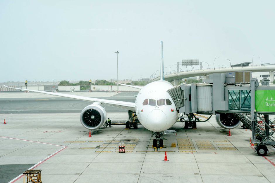 White airplane docked at terminal with jet bridge on a cloudy day.