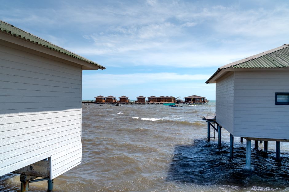 Wooden stilt houses on a sunny coastal shore, nestled above the ocean waves.