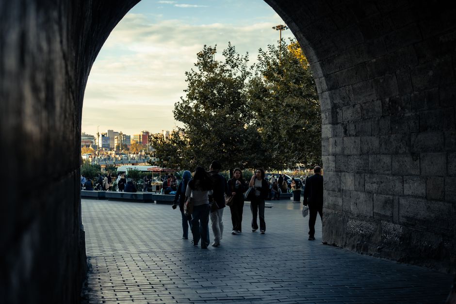 People walking through a stone archway with a cityscape backdrop at sunset.