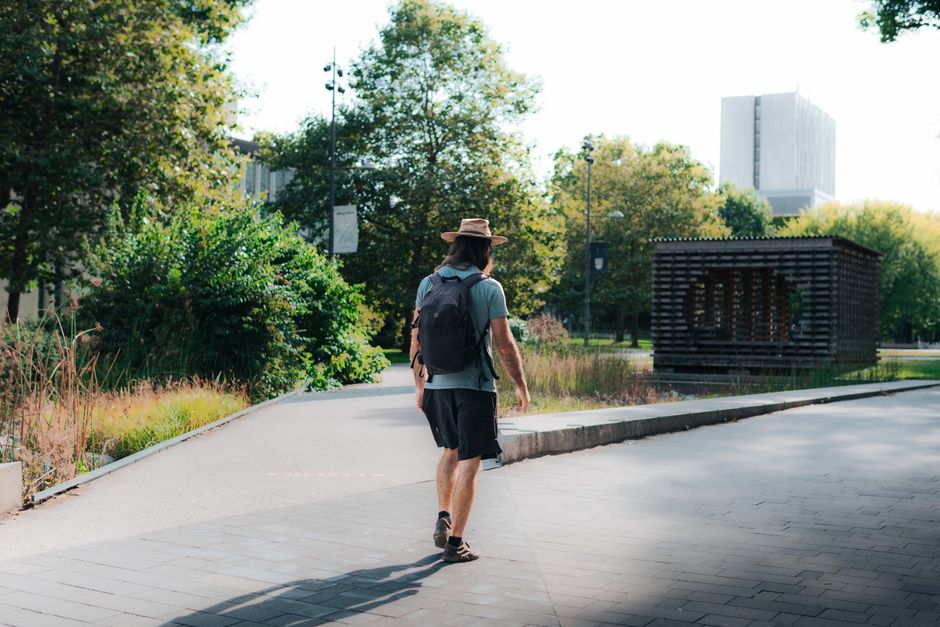 A man with a backpack walks through a sunlit park in Vancouver, Canada.