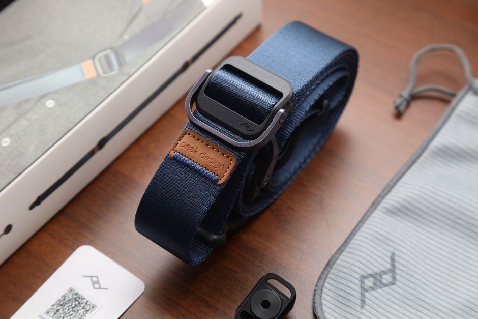 A detailed look at a Peak Design camera strap and accessories on a wooden table.