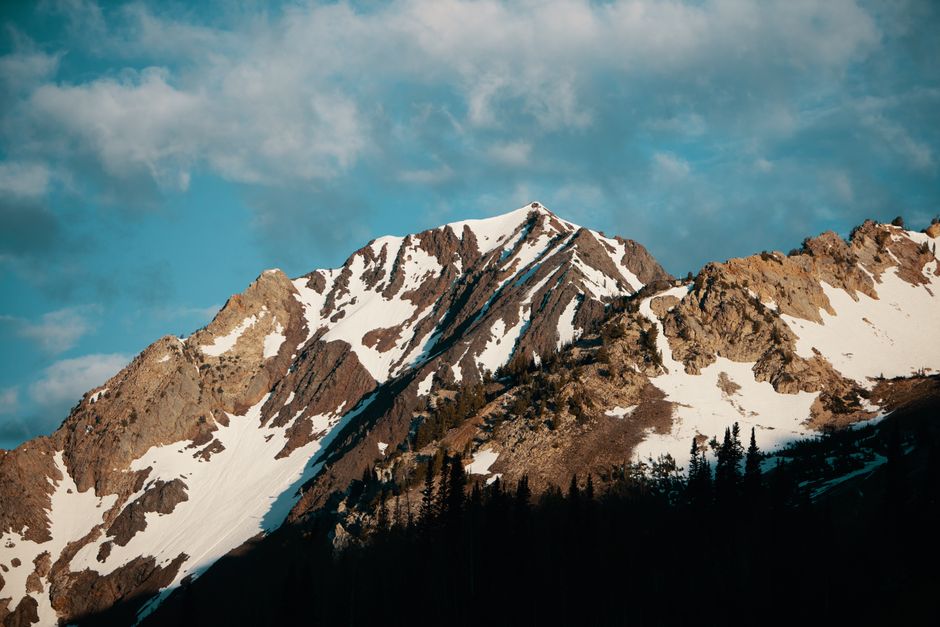 Majestic snow-covered mountain with rocky peaks under a partly cloudy sky, epitomizing rugged natural beauty.