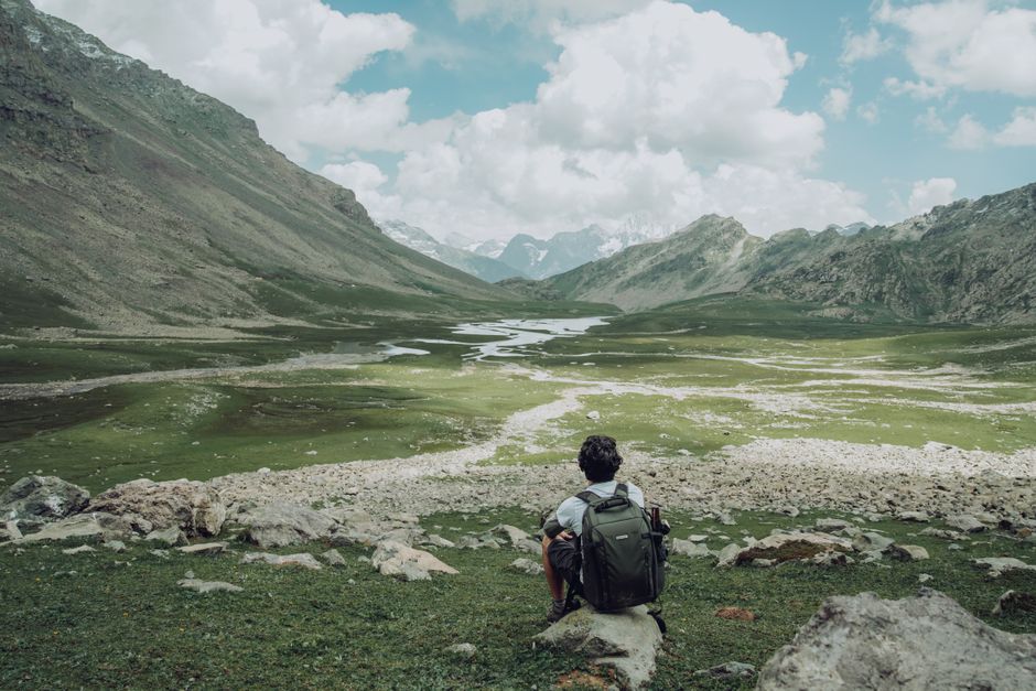 A lone traveler admires a picturesque mountain landscape during daytime, showcasing nature's beauty.
