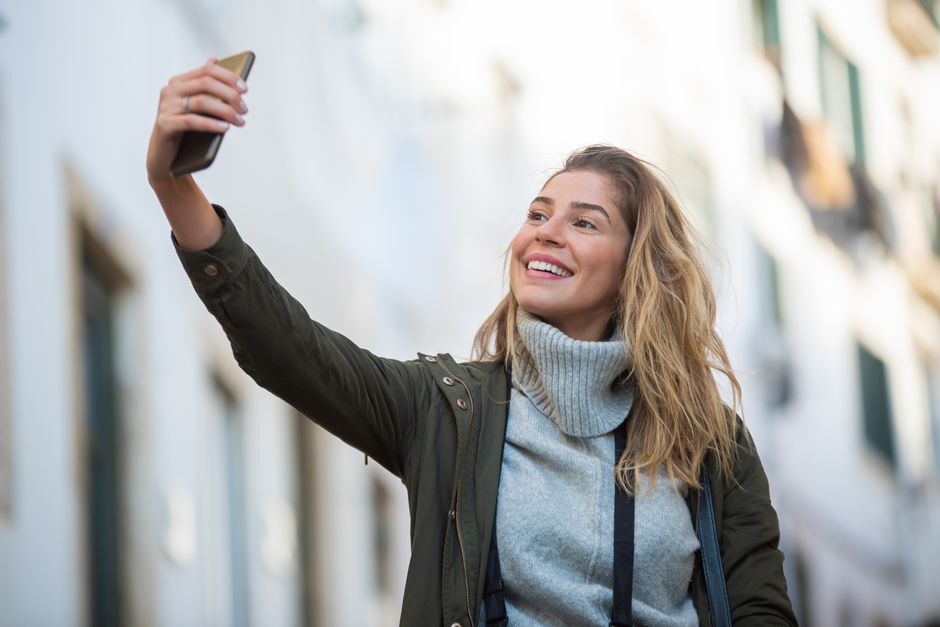 Smiling woman takes a selfie on an urban street, capturing a joyful moment outdoors.