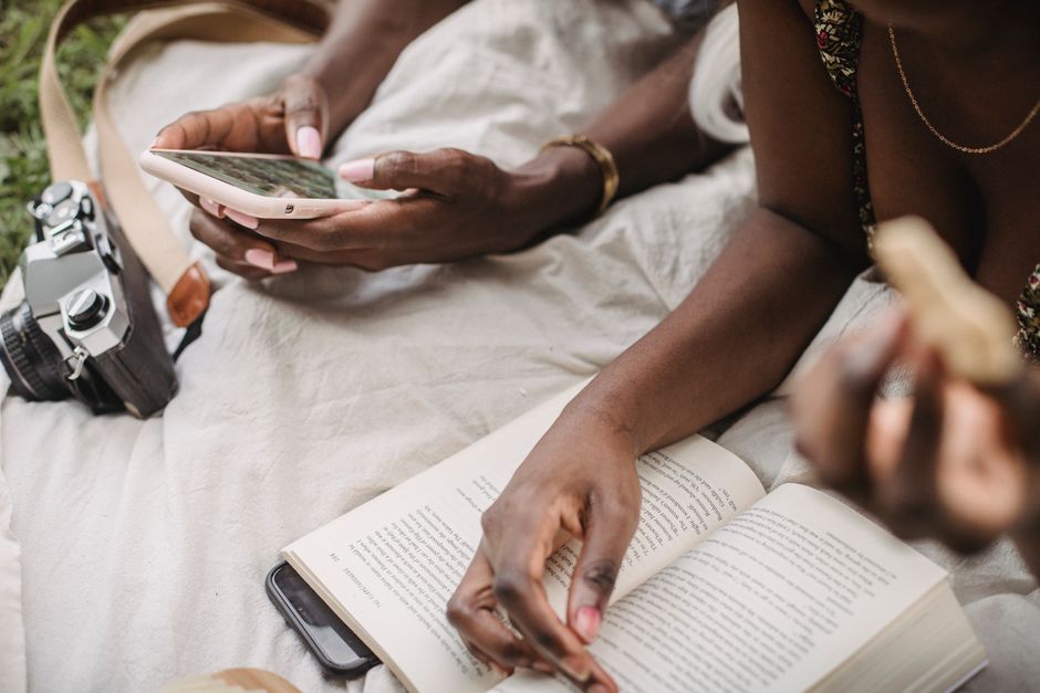 Close-up of people reading and using a smartphone outdoors, highlighting leisure and technology.