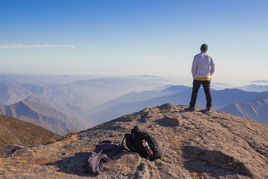 A man stands on a mountain in Peru, overlooking the Andes with a backpack nearby, capturing adventure and wanderlust.