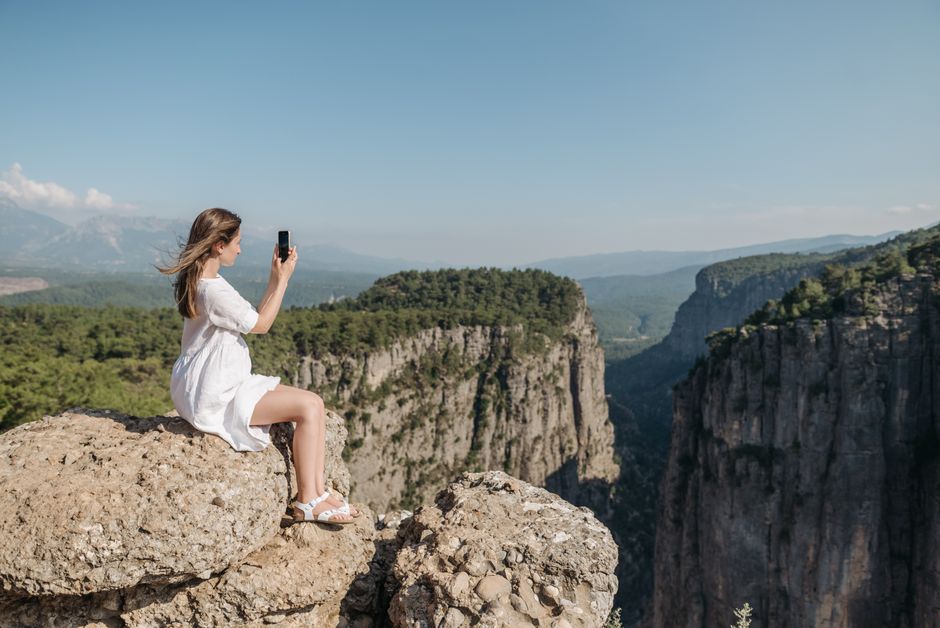 A woman in a white dress takes a photo of a stunning canyon view during a sunny day hike.