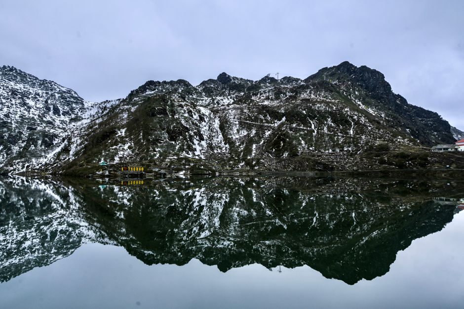 Serene reflection of snow-dusted mountains in Tsomgo Lake, Sikkim. A breathtaking winter landscape.
