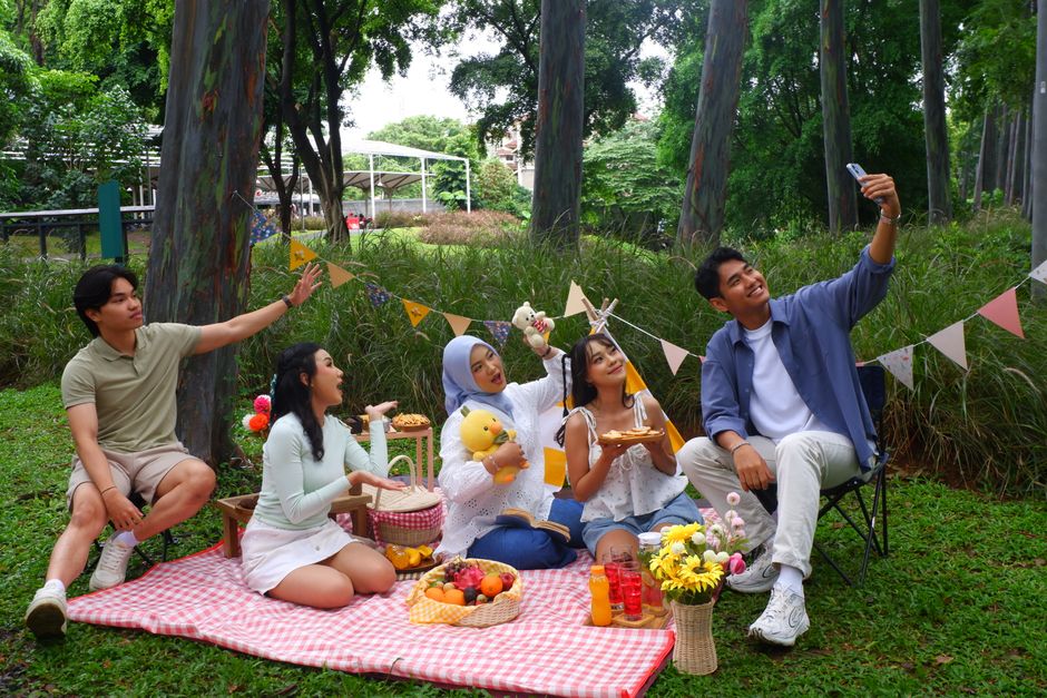 Group of friends enjoying a picnic in a lush park setting, Jakarta, Indonesia.