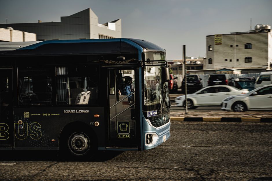 Public transport bus driving in Kuwait City, showcasing urban transit and vehicles.
