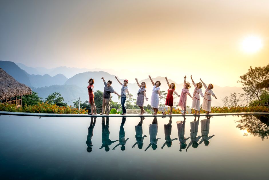 Group of happy women in colourful summer clothes raising arms in freedom standing at still water in summer evening