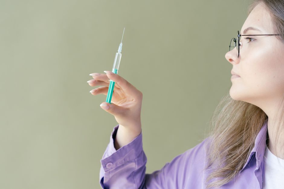 Caucasian woman in glasses holding a syringe, examining it carefully.