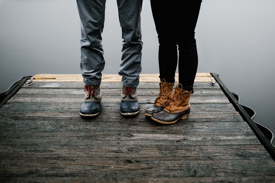 A couple stands on a dock in bean boots, showcasing fashion and footwear style.