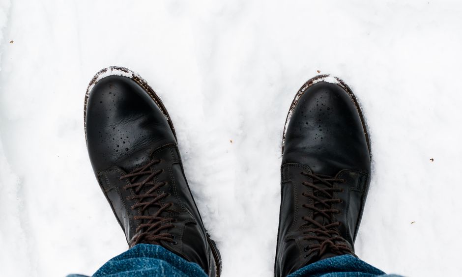 A pair of black leather boots stand in fresh snow, captured in Oslo during winter.