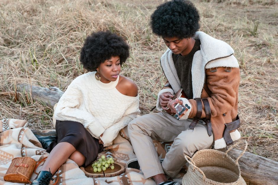 Fashionable couple with afro hair enjoying a picnic in nature with a ukulele.