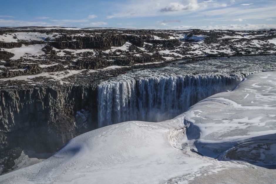 Stunning view of a majestic waterfall surrounded by icy terrain under a clear blue sky, perfect for nature and travel themes.